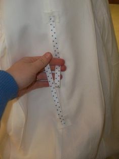 a person is holding some scissors in their hand and sewing something on the back of a white shirt