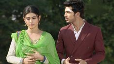 a man standing next to a woman wearing a green sari and holding her belly