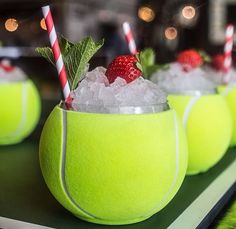 three tennis balls with strawberries and mint garnish in them on a table