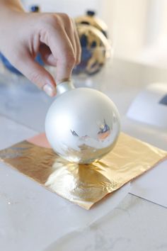 a person's hand reaching for a white ball on top of a piece of gold foil