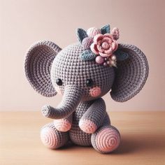 a crocheted elephant sitting on top of a wooden table next to a pink wall