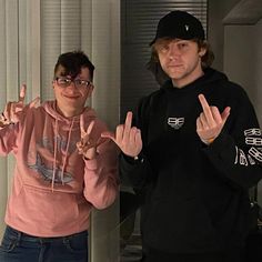 two young men standing next to each other in front of a window holding their hands up