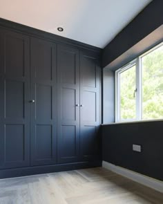 an empty room with black painted walls and wood flooring on the far wall is a window that looks out onto trees