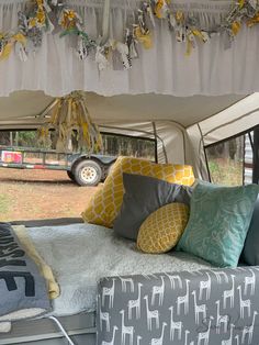 the interior of a camper is decorated with yellow and gray pillows, blue throw pillows, and white curtains