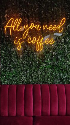 a red couch sitting in front of a neon sign that says all you need is coffee