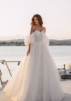 a woman in a wedding dress standing on a dock near the water with her hand on her hip