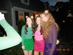 three girls are standing in front of a house at night with their arms around each other