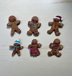 six gingerbread men and one woman wearing santa's hat are arranged on a white surface