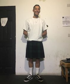 a man standing in front of a white wall wearing a black and white kilt