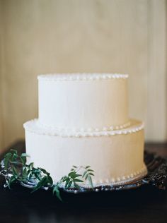 a three tiered white cake sitting on top of a wooden table with greenery