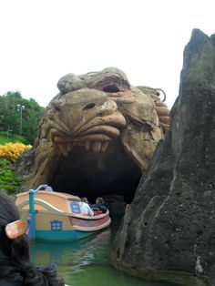 a boat is in the water near a large stone lion's head at an amusement park