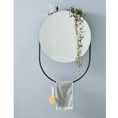 a round mirror hanging on the wall next to a towel rack with plants in it