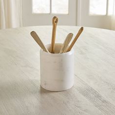 a white cup filled with wooden utensils on top of a table