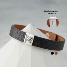 a close up of a black and white leather bracelet with an engraving on the clasp