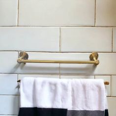 a towel rack with two towels hanging on it's side in front of a white tiled wall