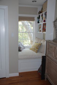 a window seat in the corner of a room next to a dresser and chest of drawers