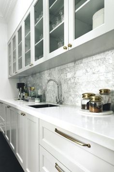 a kitchen with white cabinets and marble counter tops, along with brass pulls on the drawers