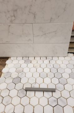 a white marble bathroom with hexagonal tiles and a metal handle on the floor