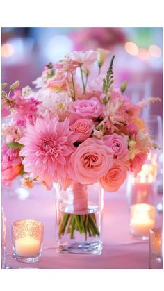 a vase filled with pink flowers on top of a table next to candles and glasses