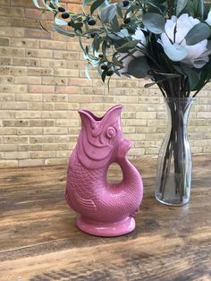 a vase filled with flowers next to a pink fish shaped vase on a wooden table