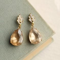 These beautifully detailed art deco earrings feature a stylised crystal geometric design with an amazing, ivory champagne coloured glass stone. The champagne teardrop has a very subtle, matte finish with gold glowing from behind, which takes on an beautiful sheen in certain lights. This irridescence with the delicate ivory colours of the glass looks great with the strong, classic art deco design of the gold brass. The drop and settings are solid brass. The earrings have a post fastening with but Gold Art Deco Clip-on Earrings For Formal Occasions, Vintage Teardrop Crystal Earrings For Formal Occasions, Vintage Crystal Teardrop Earrings For Formal Occasions, Formal Art Deco Dangle Bridal Earrings, Formal Art Deco Bridal Dangle Earrings, Art Deco Dangle Bridal Earrings For Formal Occasions, Vintage Clip-on Bridal Earrings For Wedding, Vintage Teardrop Bridal Earrings For Wedding, Formal Art Deco Clip-on Earrings