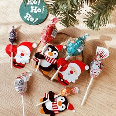 several lollipops decorated as santa claus and penguins on a wooden table next to a christmas tree