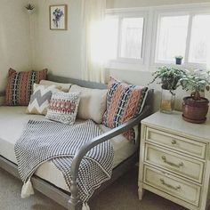 a day bed with pillows and blankets on it in front of a window next to a dresser