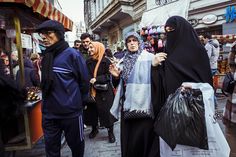 two women in burkas are walking down the street with shopping bags on their heads