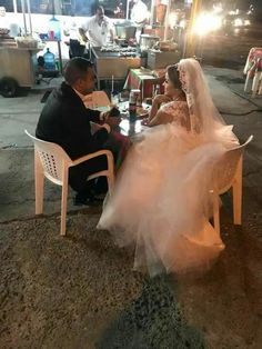 a bride and groom sitting at a table in the middle of an outdoor market area