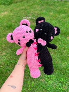 two crocheted teddy bears in pink and black are held up by a person's hand