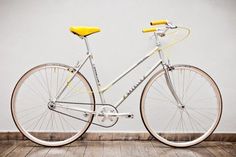 a white and yellow bicycle parked on top of a wooden floor next to a gray wall