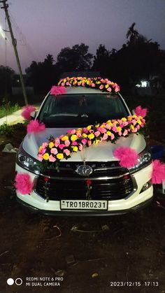 a white car with pink and yellow flowers on it's front end, parked in the street