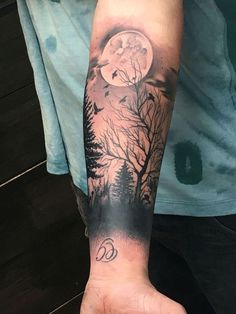 a man's arm with a full moon and trees tattoo on the left forearm