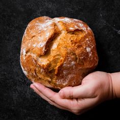 a person holding a loaf of bread in their hand on a black surface with some powdered sugar