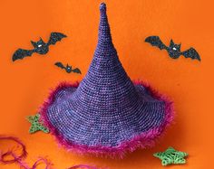 a crocheted witches hat with bat decorations on an orange background and purple yarn