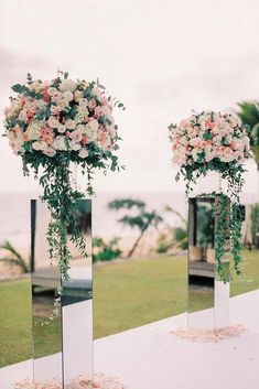 three tall vases filled with flowers sitting on top of a white cloth covered table