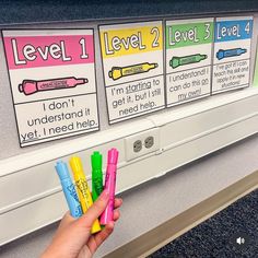 a hand is holding four markers in front of a bulletin board