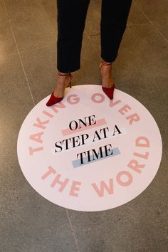 a woman standing in front of a sign that says taking over the world one step at a time