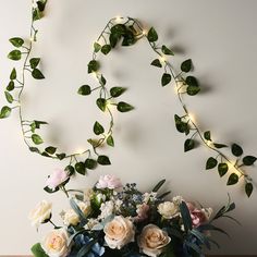 a vase filled with flowers and greenery next to a string of lights on the wall