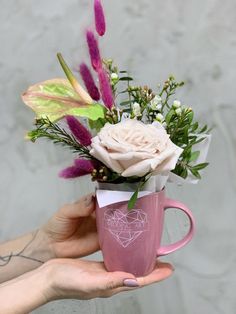 a person holding a pink coffee cup with flowers in it and purple feathers on the side