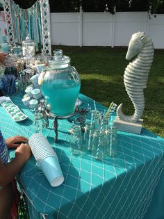 a blue table topped with lots of bottles and glasses next to a seahorse statue