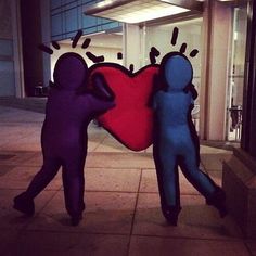 two people standing next to each other in front of a building holding a large heart