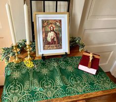 a table topped with a framed painting next to two candles and a small red box