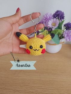 a hand holding a tiny pikachu keychain with flowers in the background