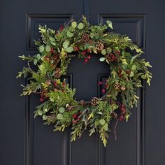 a christmas wreath on the front door of a house with pine cones, holly and berries