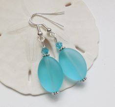 two blue glass tears hang from silver earwires on a white sand dollar