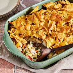 a green casserole dish with tortilla chips and salsa in it on a table