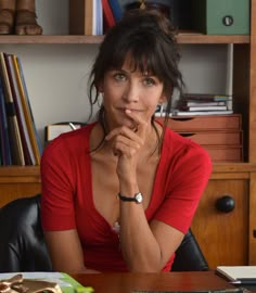 a woman sitting at a desk with her hand on her chin and looking to the side