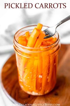 a jar filled with pickled carrots on top of a wooden tray next to a spoon