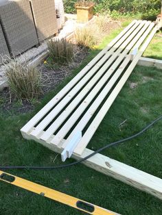 a wooden bench sitting in the grass next to a garden hose and some plants on top of it